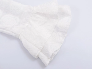 Close-up of white textured fabric sleeve with ruffled cuffs and elegant floral patterns