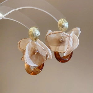 Detail of floral chiffon earrings with resin ring and gold textured stud in soft light