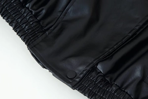 Detail of black faux leather jacket featuring elastic pleats and matte snap button