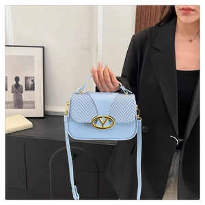 Detail of light blue crossbody bag featuring chevron fabric flap and gold V-buckle