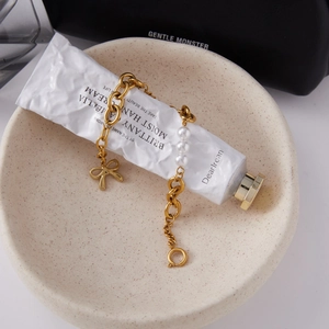 Close-up of gold chain bracelet with bow charm and imitation pearls on white tube