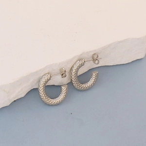 Detail of silver oval hoop earrings with snake scale texture on white stone base