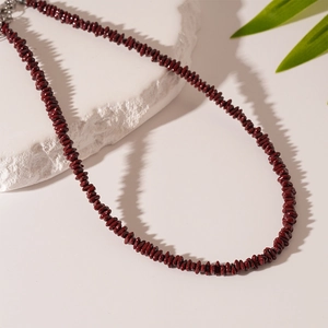 Detail of dark red irregular beaded necklace on stone surface with a green leaf