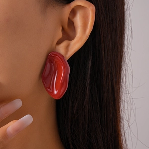 Close-up of a model wearing large red irregular geometric resin earrings with a glossy finish