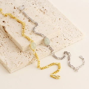 Close-up of gold and silver Figaro chains with oval aventurine stones on stone
