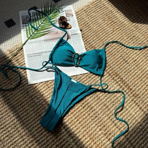 Detail eines dunkelgrünen Bikinis mit Metallring-Akzent und Strukturstoff auf Strohmatte