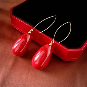 Elegant gold drop earrings with glossy red waterdrop pearls on luxury display