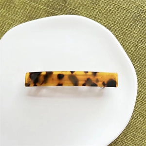 Close-up of tortoise shell acetate hair clip with metal spring on a white ceramic plate