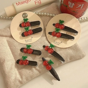 Sparkly red cherry hair clips with green leaves set on a minimalist beige linen background