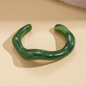 Close-up of wavy dark green acrylic open bangle with marble texture and polished finish