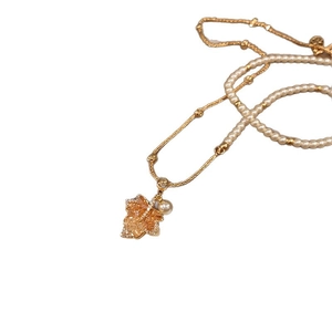 Collier avec pendentif feuille d'érable dorée, cristaux et perles sur fond blanc