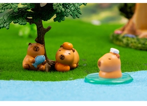 Miniature capybara resin figures with orange and blue fish on a green lawn scene
