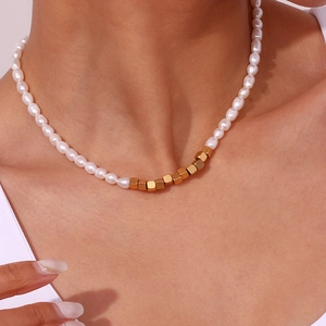 Close-up of beaded necklace with white pearls and matte gold cube accents on model