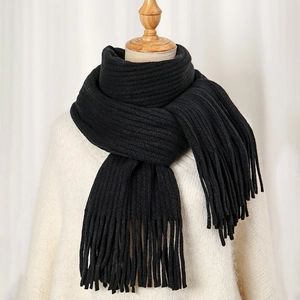 Detailaufnahme eines schwarzen, dick gestrickten Winterschals mit weichen Quastenfransen