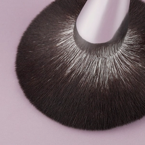 Large fluffy powder brush with soft bionic bristles and solid wood handle on lilac background