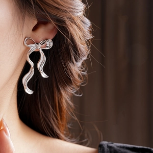 Gros plan macro d'une boucle d'oreille nœud argenté sur mannequin, bijou minimaliste