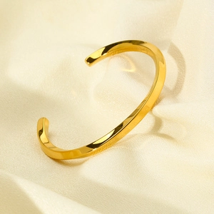 Detail of twisted 18k gold plated stainless steel open bangle on beige satin silk fabric