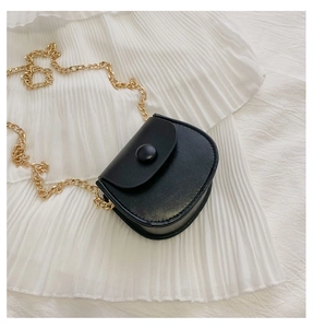 Détail du mini sac selle noir avec bandoulière chaîne dorée sur fond de tissu blanc