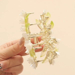 Close-up of a silver hair claw with white camellia flowers and green leaves details