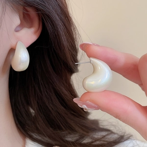 Close-up of cream-white teardrop stud earrings with subtle pearlescent luster
