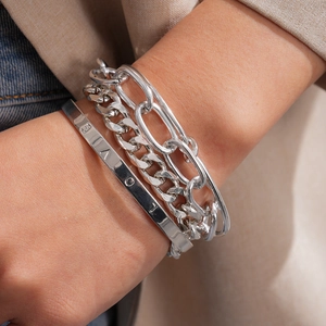 Dichtbij van een zilverkleurige vierdelige ketting en gegraveerde LOVE-armband om een pols.