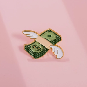 Close-up of funny flying dollar enamel pin with white wings and golden metal edges