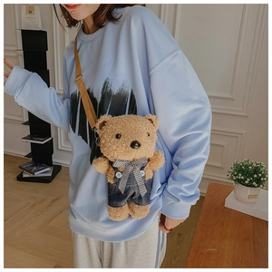 Detail of cute brown teddy bear plush crossbody bag wearing denim overalls and a plaid bow