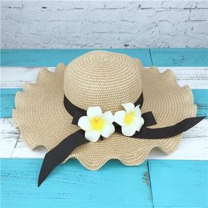 Detail of beige straw sun hat with wave brim, black ribbon, and tropical plumeria flowers