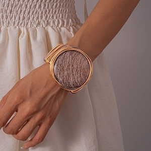 Detailed close-up of a gold woven resin cuff bracelet with a large textured round disc