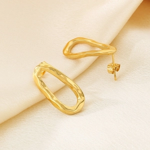 Macro detail of gold irregular molten lava texture stud earrings on silk fabric