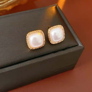 Detail of square gold plated earrings featuring a lustrous pearl center and zircon stones