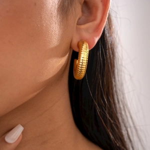 Close-up of golden C-shaped ribbed earrings with spiral texture on a female model