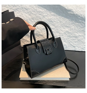 Detail of black crocodile texture leather handbag with square metal buckle and curved handle