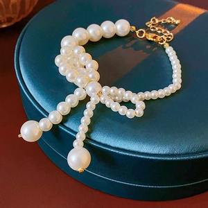 Dettaglio di bracciale con fiocco di perle e finiture dorate su portagioie verde scuro