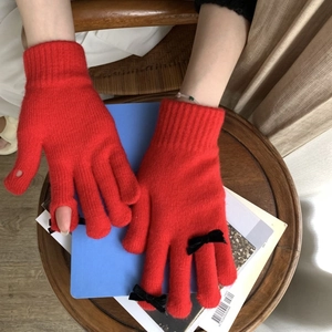 Detail of red knitted gloves with black bow accents and practical touchscreen finger openings
