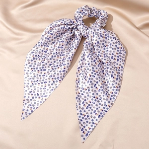 Close-up of silk ribbon scrunchie with blue evil eye pattern on golden fabric