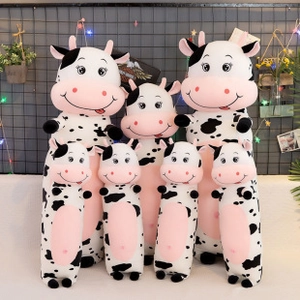 Plush cow toys in various sizes with black spots and pink accents on a grid wall background