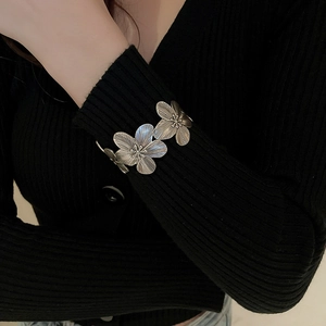 Detail of vintage silver flower cuff bracelet worn over a black knit sweater sleeve