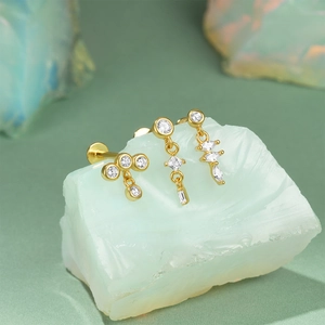 Close-up of gold cartilage studs with green zircon and diamond-shaped floral lace patterns