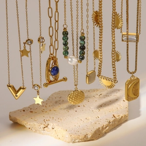 Close-up of gold stainless steel necklaces with pearl and sunburst pendants on stone