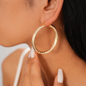 Close-up of a model wearing gold geometric spiral earrings with textured finish