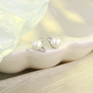 Macro shot of cute silver cat ear pearl earrings on a white porcelain decorative tray
