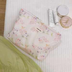 Floral print cosmetic bag in cream with purple flowers and zipper closure on a white mat