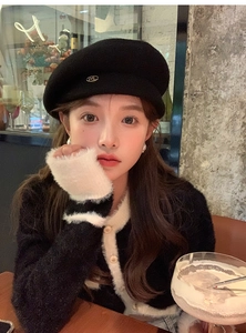 Detail of a chic black wool beret with metal logo paired with a fuzzy cardigan