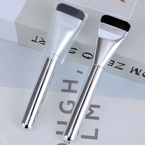 Detail of silver makeup brushes with black bristles and a protective cap on the brush head