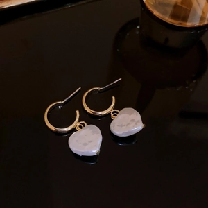 Detail of gold C-shaped hoop earrings with irregular white heart-shaped pearl pendants