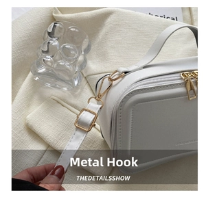 Detail of white suitcase crossbody bag with golden metal hooks and adjustable strap