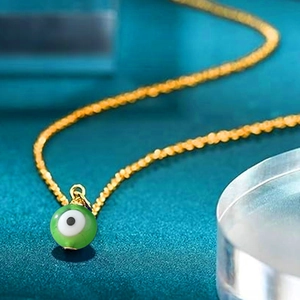 Detailed close-up of a green evil eye pendant with a golden twisted chain necklace