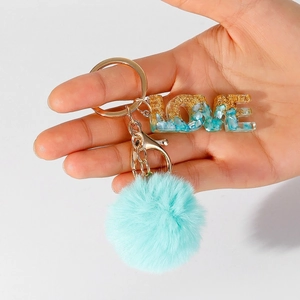 Detailed macro view of LOVE resin letter keychain with gold flakes and blue fur pompom