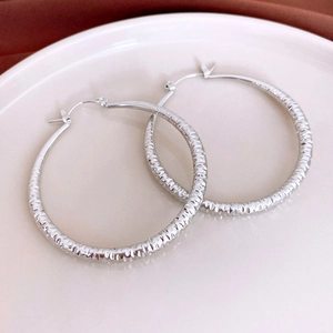 Macro detail of silver hoop earrings featuring textured diamond-cut stripe patterns